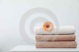 Stack of fresh towels with flower on table against white background