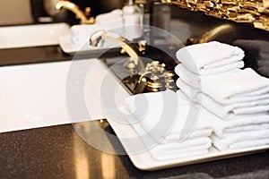A stack of fresh white towels in the hotel`s luxurious bathroom. A gold faucet, mirror and marble sink in a public restroom of an
