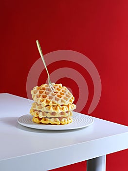 Stack of freshly made Belgian waffles, topped with a small spoon, on a white plate