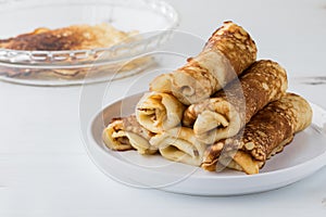 A stack of freshly made crepes on a plate with unrolled ones in behind.