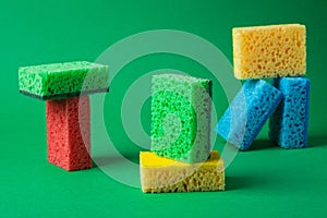 Stack geometric blocks construction abstract sponges in red, yellow, blue colors, on green paper background, copy space