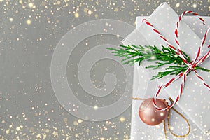 Stack of gift boxes wrapped in white paper tied with red twine green twig golden ball on gray background with sparkling glitter
