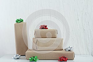 Stack of gifts in kraft paper with bow of green, red and silver colors. Plaster wall. Copy space, mock up