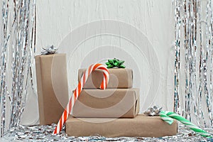 Stack of gifts in kraft paper with bow of green, red and silver colors. Tinsel on a white background Christmas candy cane. Plaster