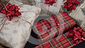 Stack of gifts wrapped in festive Christmas paper with season specific print, red shiny bows and red metallic tinsel string rope