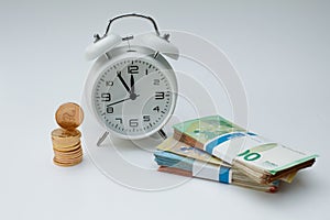 A stack of gold coins stands next to an alarmclock