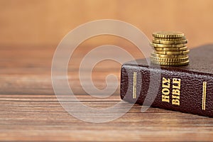 Stack of golden coins on top of holy bible book on a wooden background