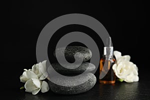 Stack of grey spa stones, flowers and oil on black table