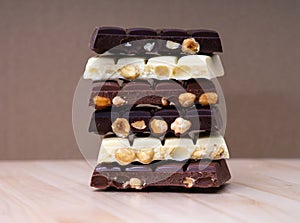 Stack of half chocolate bars with hazelnuts - milk chocolate, dark chocolate and white chocolate on wooden background
