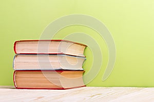 Stack of hardback books, diary on wooden deck table and green background. Back to school. Copy Space. Education