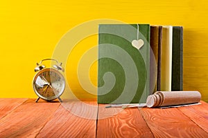 Stack of hardback books, diary on wooden deck table and yellow background. Back to school. Copy Space. Education