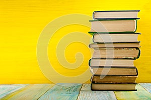 Stack of hardback books, diary on wooden deck table and yellow background. Back to school. Copy Space. Education