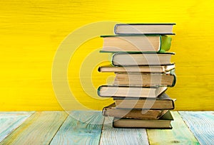 Stack of hardback books, diary on wooden deck table and yellow background. Back to school. Copy Space. Education