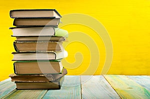 Stack of hardback books, diary on wooden deck table and yellow background. Back to school. Copy Space. Education