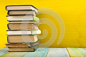 Stack of hardback books, diary on wooden deck table and yellow background. Back to school. Copy Space. Education