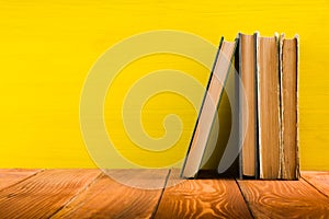 Stack of hardback books, diary on wooden deck table and yellow background. Back to school. Copy Space. Education