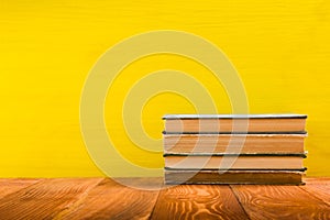 Stack of hardback books, diary on wooden deck table and yellow background. Back to school. Copy Space. Education