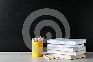 Stack of hardcover books and color pencils on table against black background