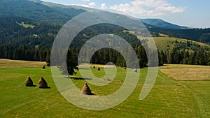 Stack of hay on a green meadow on hillside near the mountain village in sunset light