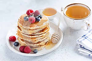 Stack of healthy oat pancakes with berries, honey and cup of green tea