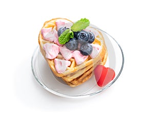 Stack of heart shaped waffles with pink cream and blueberry isolatedon white