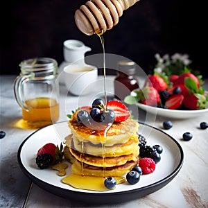 A stack of home made cottage cheese pancakes with honey, strawberries, blueberries and other berries on a dark gray background,