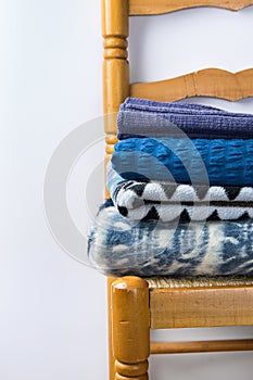 Stack of Home Warm Knitted Blue Plaids Blankets From Rough Wool Yarn Brown Beige Grey on Vintage Chair White Wall Background.
