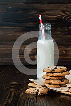 Stack of homemade chocolate chip cookies with milk on dark wooden table. Copy space background