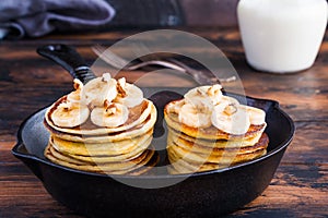Stack of homemade pancakes with banana, maple syrup and walnuts in black cast iron skillet.