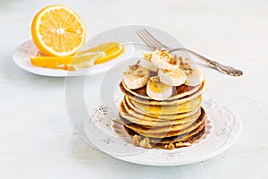 Stack of homemade pancakes with banana, maple syrup and walnuts on vintage plate.