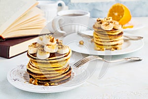 Stack of homemade pancakes with banana, maple syrup and walnuts on vintage plate.