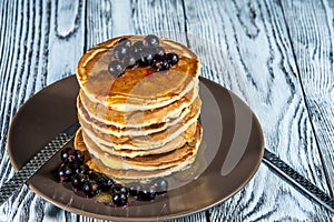 Stack of homemade pancakes with berries and honey on brown plate on rustic background