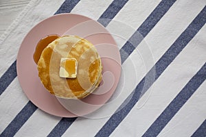 Stack of homemade pancakes with butter and maple syrup on a pink plate, top view. Overhead, from above, flat lay. Close-up. Copy