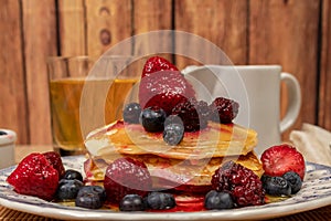 Stack of homemade pancakes prepared with blueberries, strawberries and maple syrup or honey