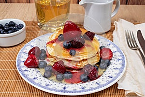 Stack of homemade pancakes prepared with blueberries, strawberries and maple syrup or honey