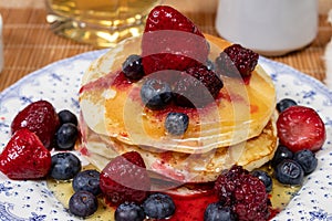 Stack of homemade pancakes prepared with blueberries, strawberries and maple syrup or honey