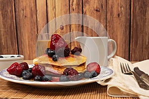 Stack of homemade pancakes prepared with blueberries, strawberries and maple syrup or honey