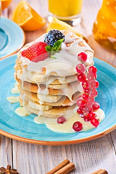 Stack of homemade pancakes with strawberrie, banana and red currant on a blue plate