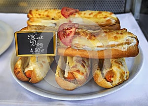 Stack of hot dogs in baguette buns covered with melted cheese on display at a local sandwich shop in Nice, France