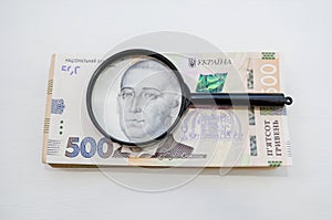 Stack of hryvnia banknotes and a magnifying glass. Light background. A lot of money. Ukrainian hryvnia. View from above.