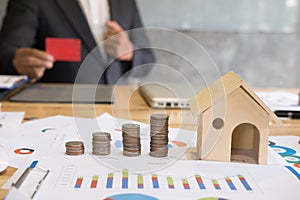 Stack of increasing coins and house model with businessman showing credit card. Investment in property, saving money for buying