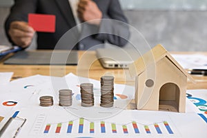 Stack of increasing coins and house model with businessman showing credit card. Investment in property, saving money for buying