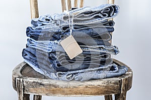 Stack of jeans with tag on wooden chair