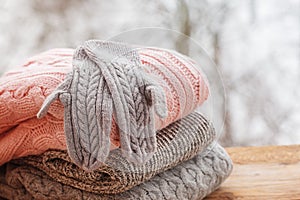 Stack of knitted clothes on wooden tableon winter nature background.