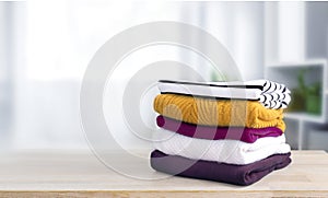 Stack of knitted jersey clothes on wooden table empty copy space. Folded knitwear, autumn colorful apparel photo