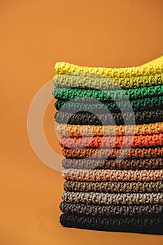 Stack of knitted material from multicolored threads on a orange background. Copy, empty space for text