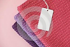 Stack of knitted material from threads of pink, red, purple colors with blank Price Tag on a pink background. Top view. Copy,
