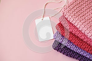 Stack of knitted material from threads of pink, red, purple colors with blank Price Tag on a pink background. Top view. Copy,