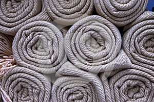 A stack of knitted white plaid folded into a roll. Several handmade woolen texture blanket in stock.