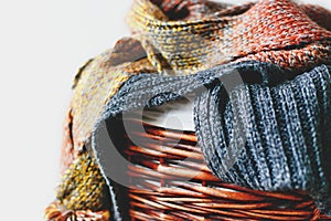 Stack of knitted winter scarfs on straw basket.